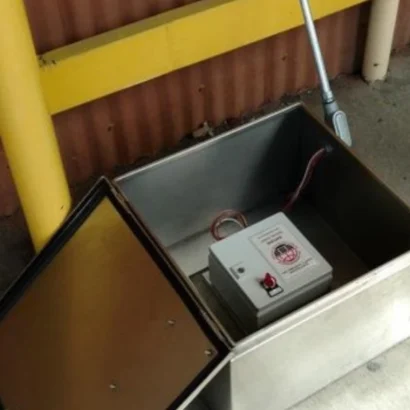 SATURN seismic switch mounted horizontally on a concrete slab inside an open stainless steel protective enclosure at an industrial site